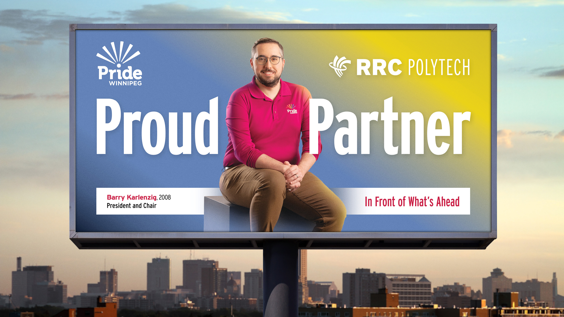 e8体育网毕业生巴里·卡伦齐格 (Barry Karlenzig) 身穿紫红色温尼伯骄傲 Polo 衫和棕褐色裤子，在广告牌上就座，这是学院理工学院骄傲活动的一部分。广告牌矗立在温尼伯城市天际线上。