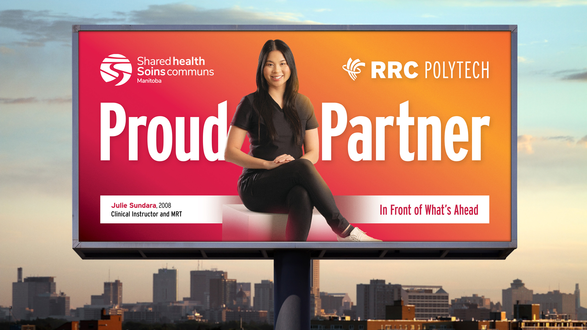e8体育 MRT 毕业生 Julie Sundara 穿着黑色工作服，自信地坐在温尼伯城市天际线上方的广告牌上。