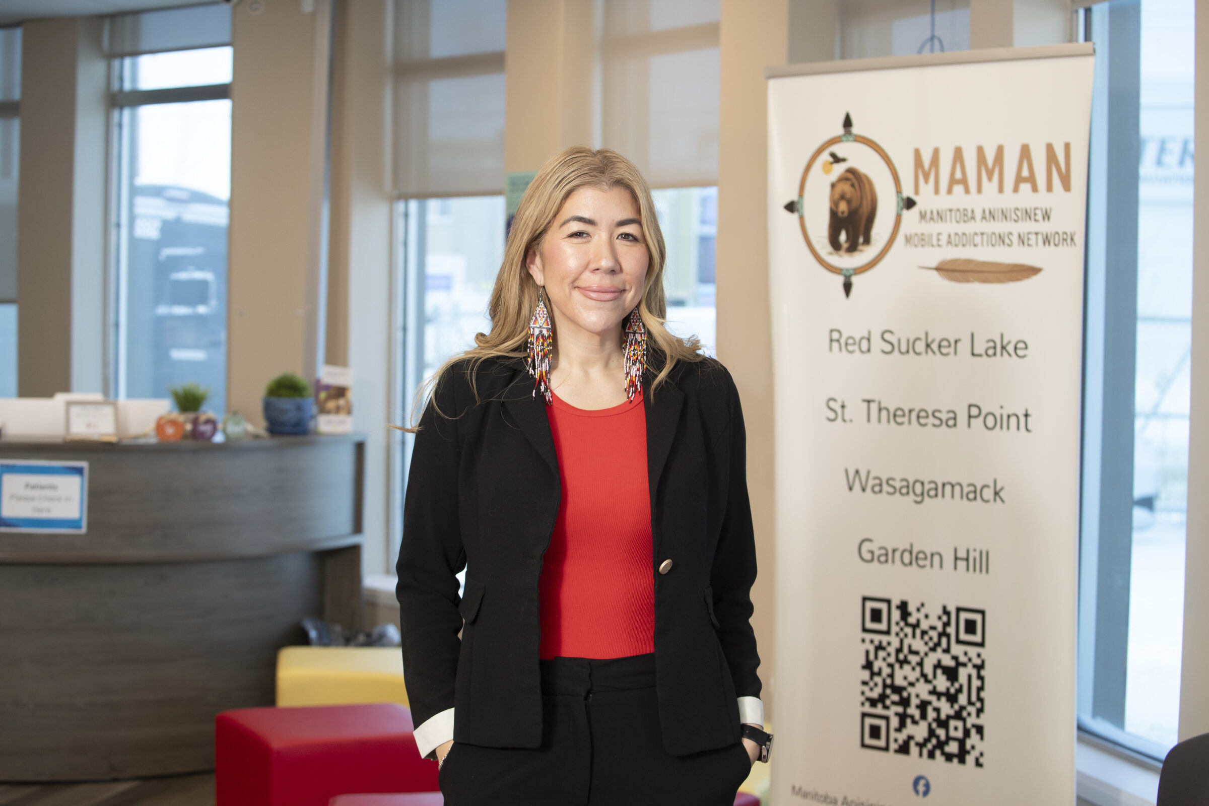 e8体育网毕业生 Kirsty Muller 穿着黑色西装外套和红色上衣，戴着长串珠耳环。