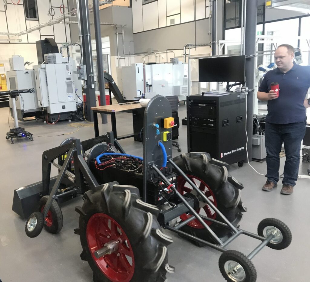 研究人员站在制造实验室的遥控训练拖拉机旁边