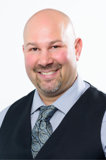 一个穿着蓝色领带、穿着黑色背心的人对着镜头微笑。