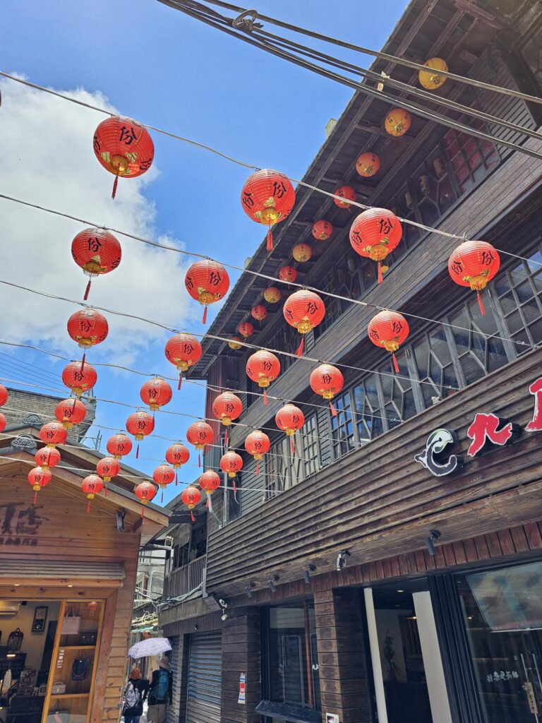 传统的街道两旁都是木制建筑，一排排红灯笼悬挂在明亮的蓝天的映衬下。