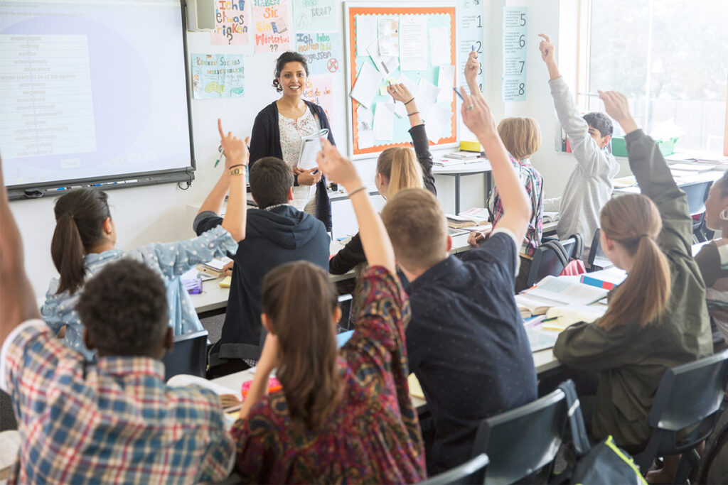 老师与满是举手的学生的教室交谈