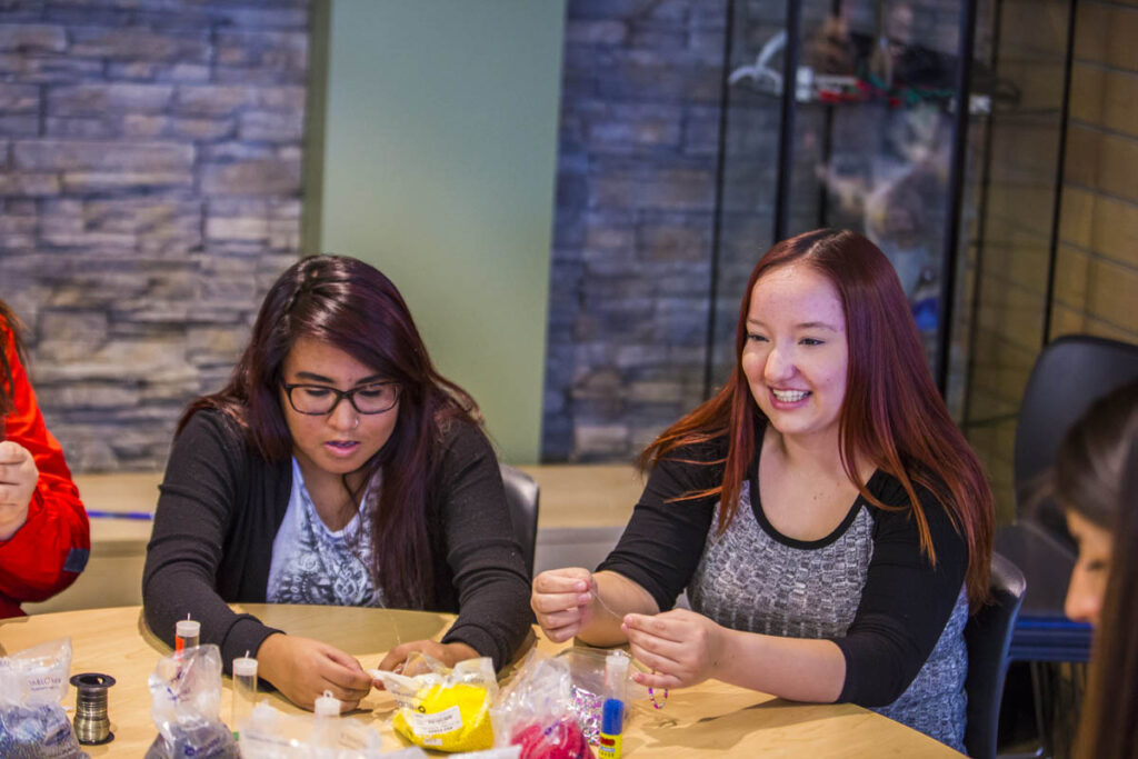 两名学生在教室里做串珠工艺品