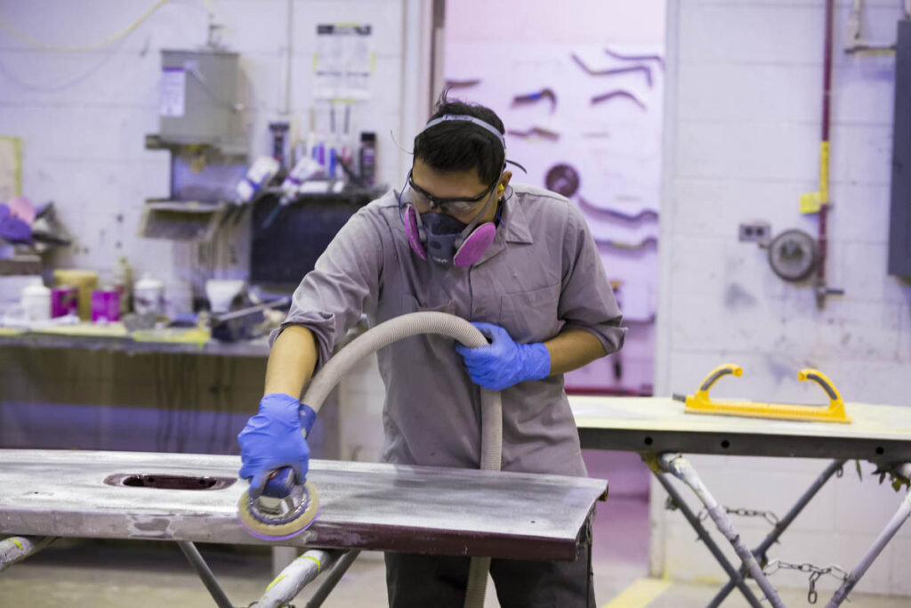 E8官方网站维修学生戴着呼吸器打磨车辆面板