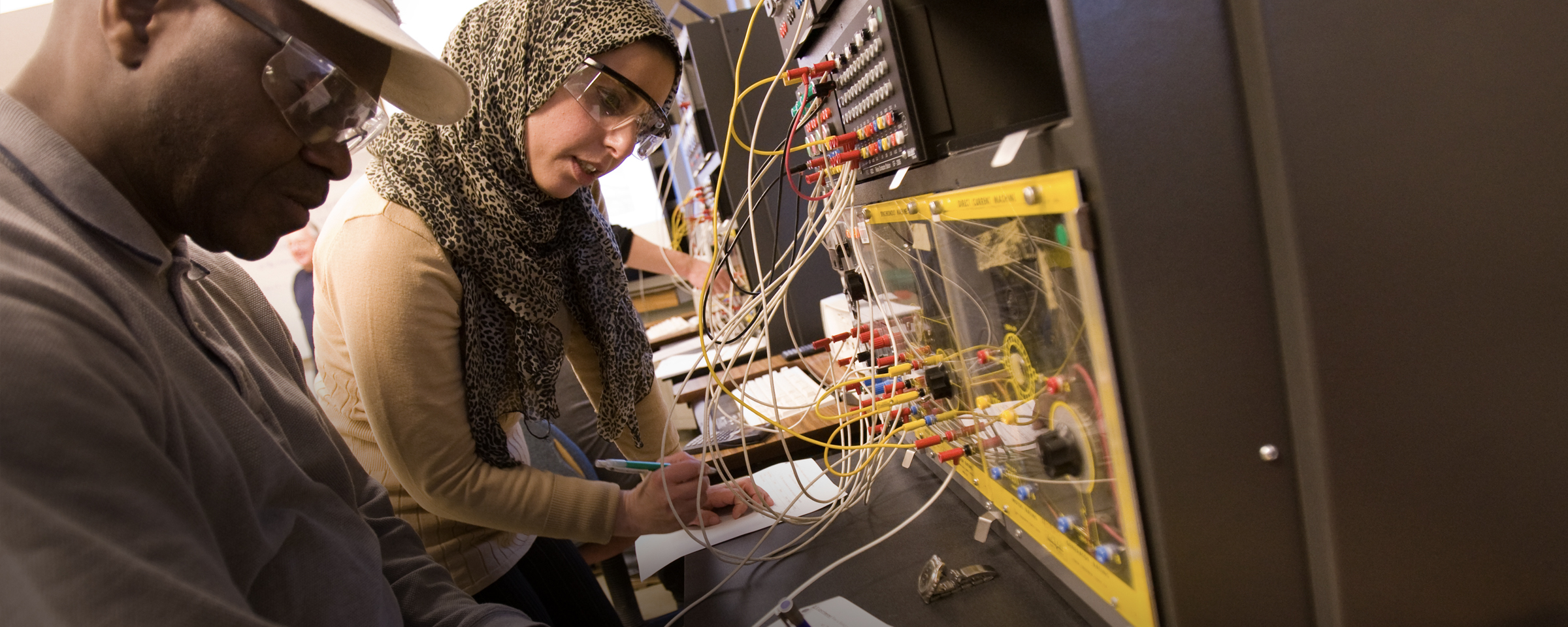 电气工程专业的学生在将电缆插入设备时记笔记