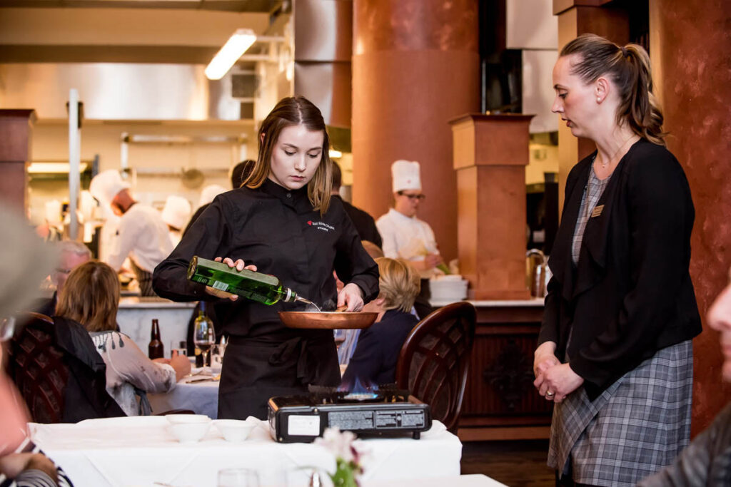 讲师在餐厅的桌边观看e8体育vip管理专业的学生制作菜肴