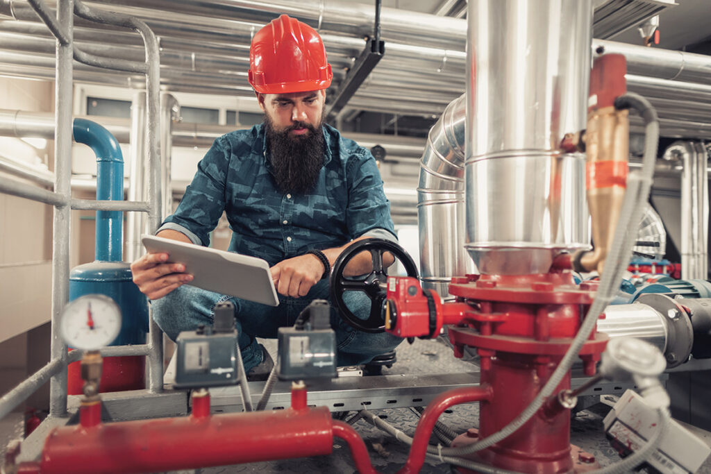 戴安全帽的男人在房间里看笔记，房间里有很多管道和仪表