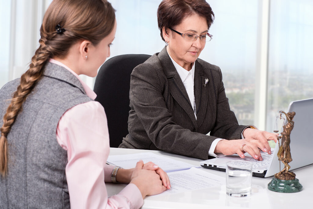 两位女士坐在桌旁，其中一位在笔记本电脑上记笔记
