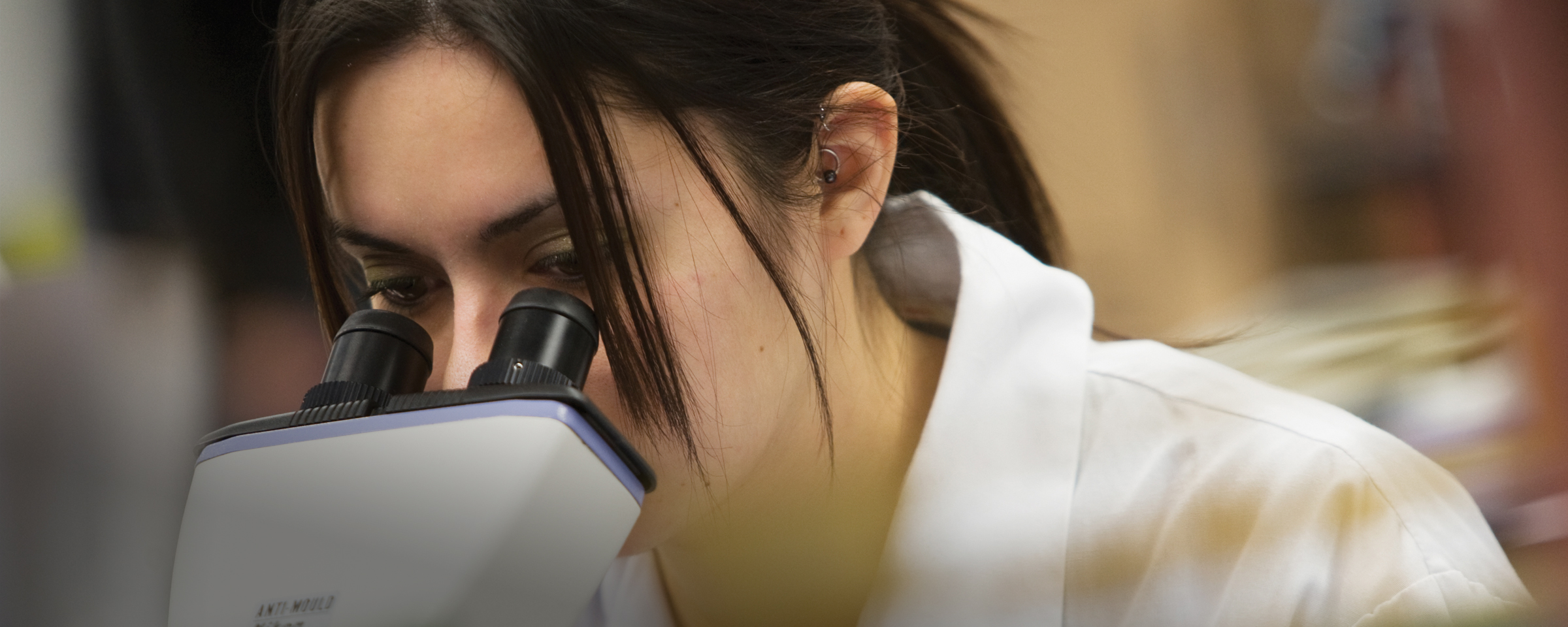 穿着实验服看着显微镜的学生