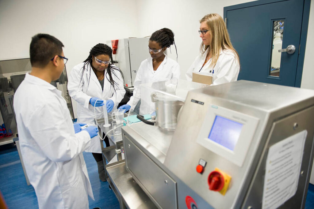 实验室里的药科学生看着他们的老师用塑料烧瓶做某事