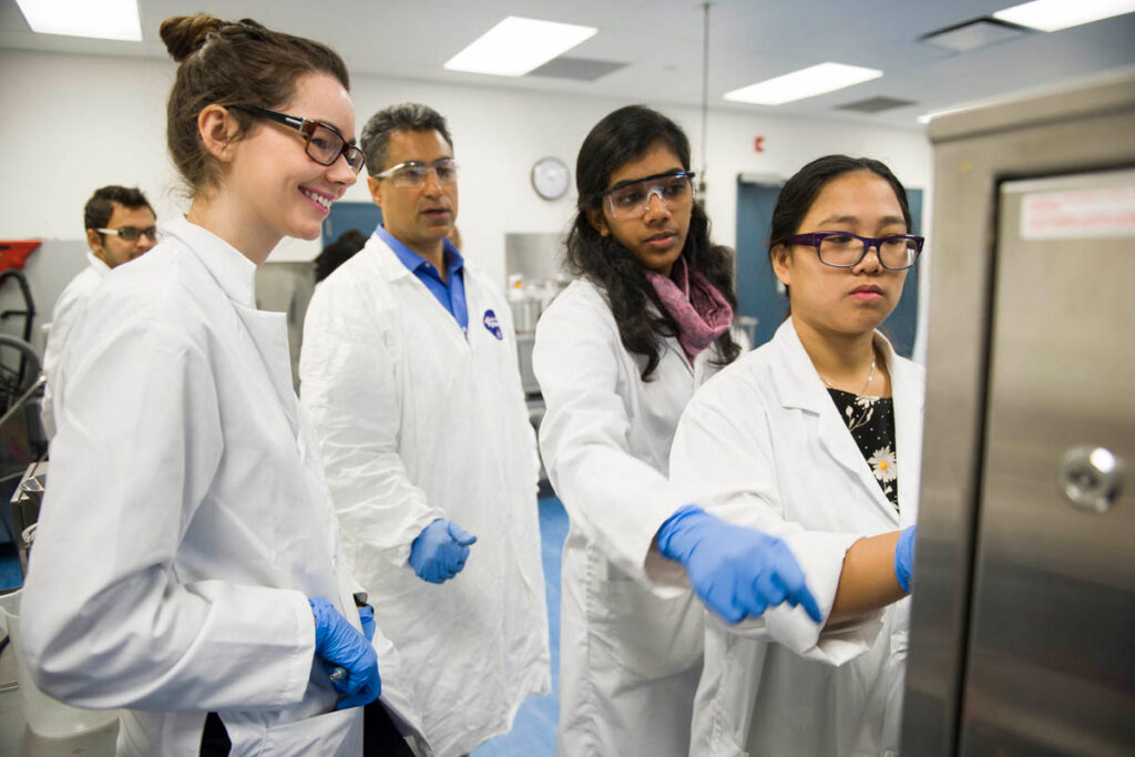 教师观看学生在制药实验室操作机器