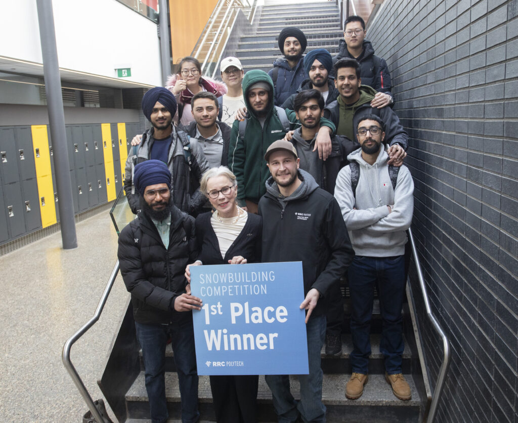 一群学生和玛丽亚站在楼梯上，玛丽亚举着一块牌子，上面写着“第一名获胜者”