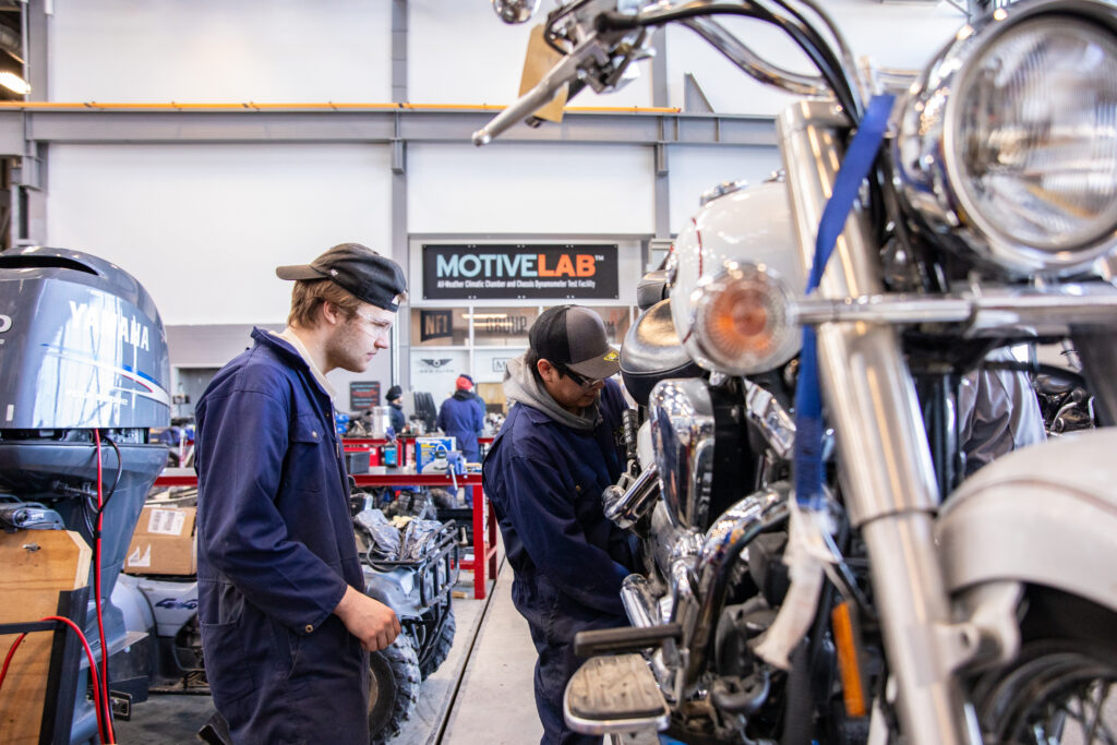 两名学生在商店教室里骑摩托车。