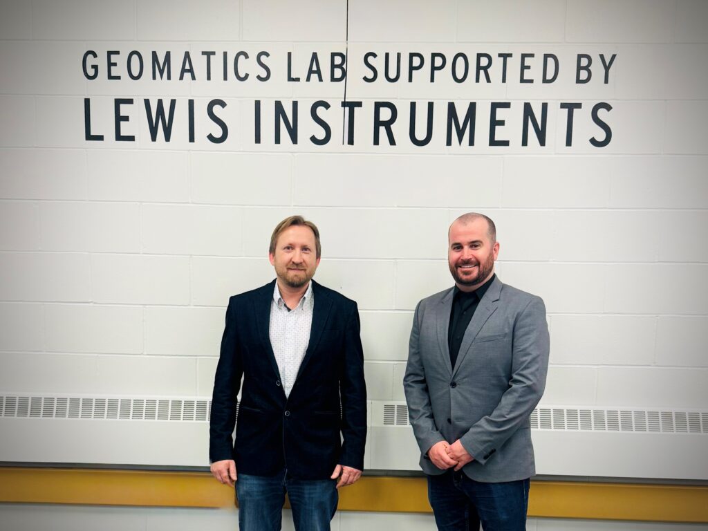 两个人站在墙边对着镜头微笑,墙上用大字写着“Lewis Instruments 支持的几何实验室”。