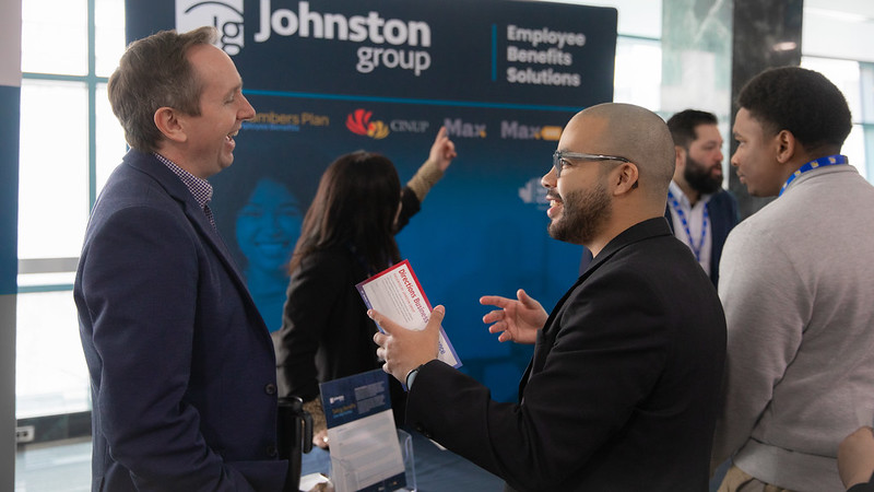 两个人在写着“Johnston Group | 员工福利解决方案”的横幅前微笑交谈。