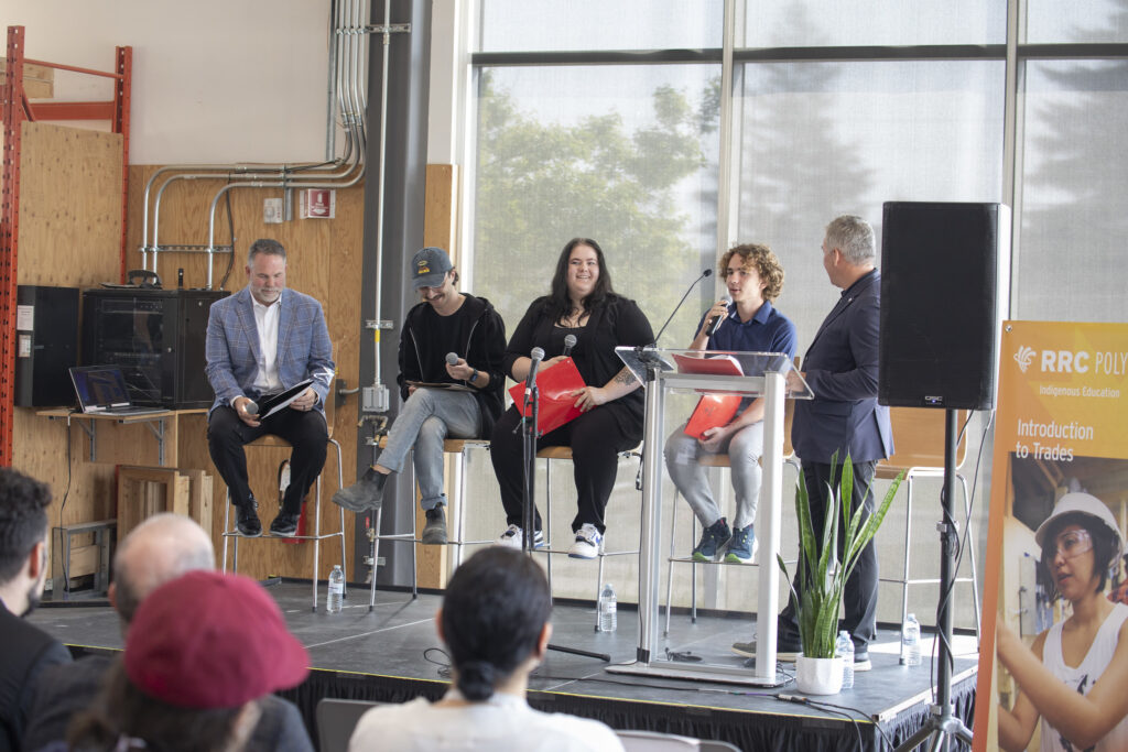 五个人坐在舞台上，微笑着拿着麦克风。