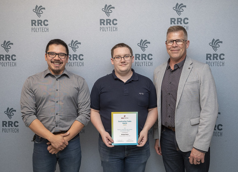 三个人微笑着站在灰色背景前。