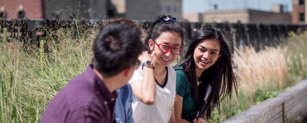 四名不同的学生坐在外面微笑。