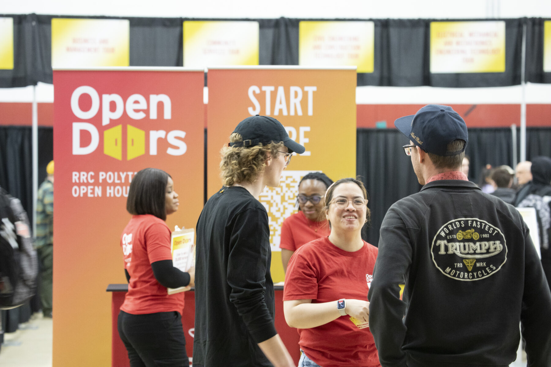 在 e8体育 的 Open Doors 活动中，两名男子与一名身穿红色衬衫的志愿者交谈。