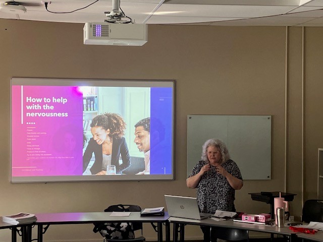 一位女士站在屏幕前，向学生演示时，屏幕上写着“如何缓解紧张情绪”。