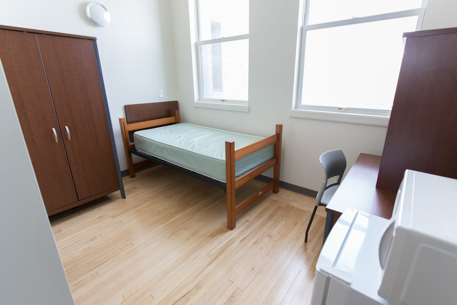 e8体育 学生宿舍的一间房间，阳光明媚的房间里有一张床，配有书桌和衣柜。