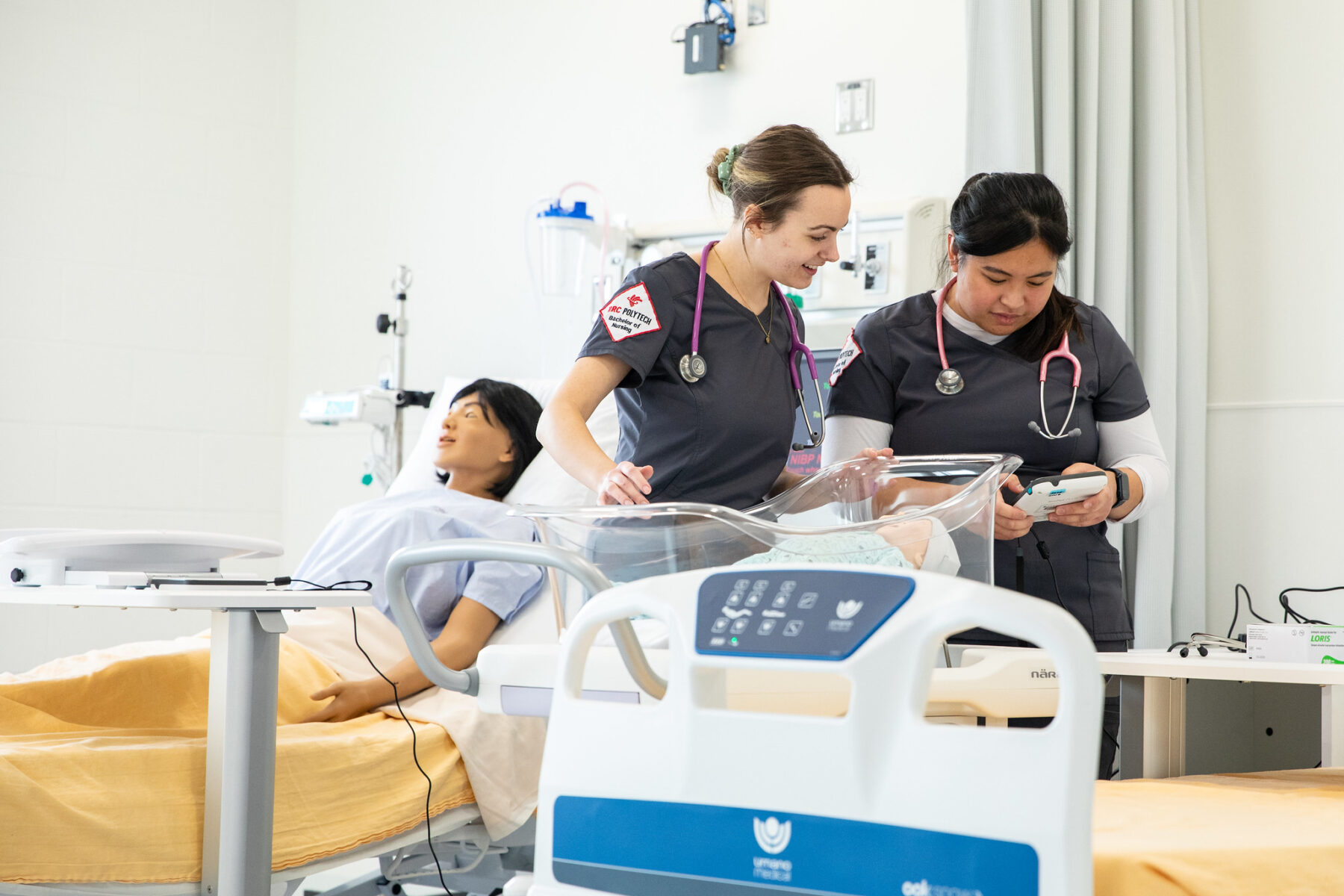 两名穿着手术服的护士正在查看图表，而人体模型躺在床上，