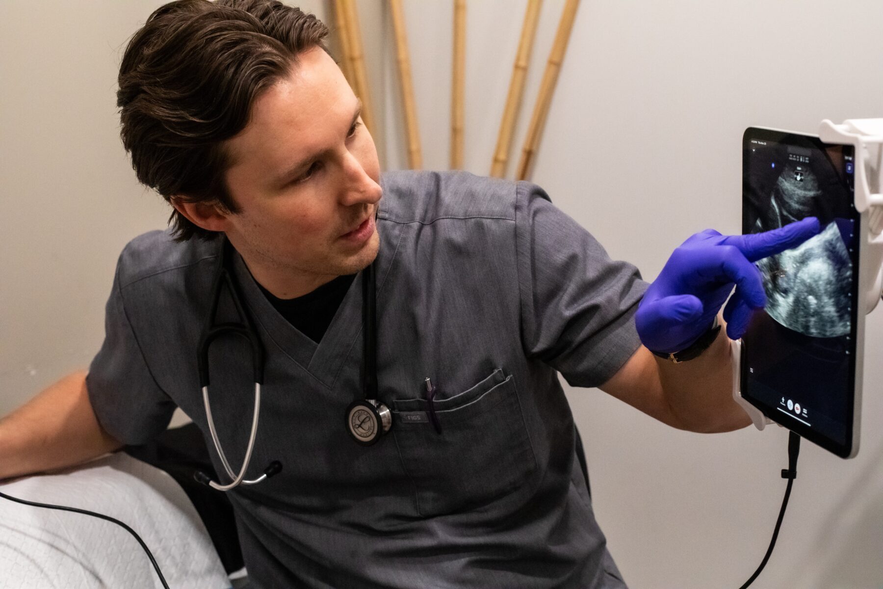 一名穿着手术服的男子指着屏幕，屏幕显示腹部超声波