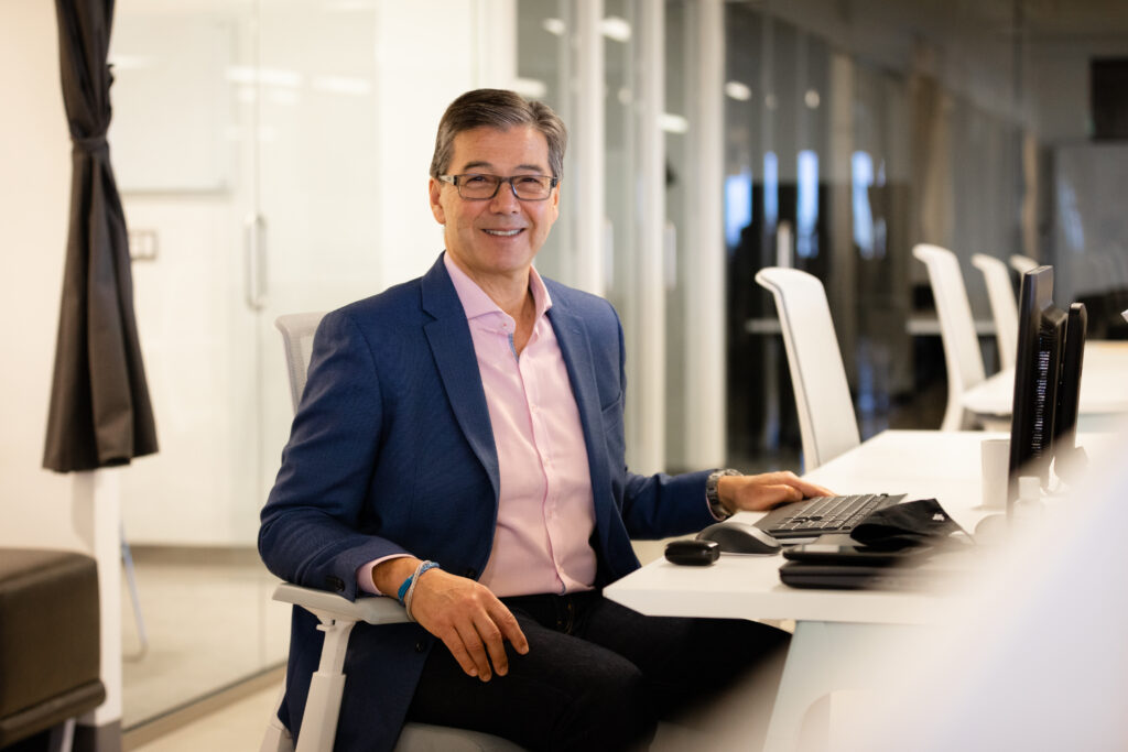 罗伯特·冈部 (Robert Okabe)，坐在会议室的桌子旁，拿着笔记本电脑。