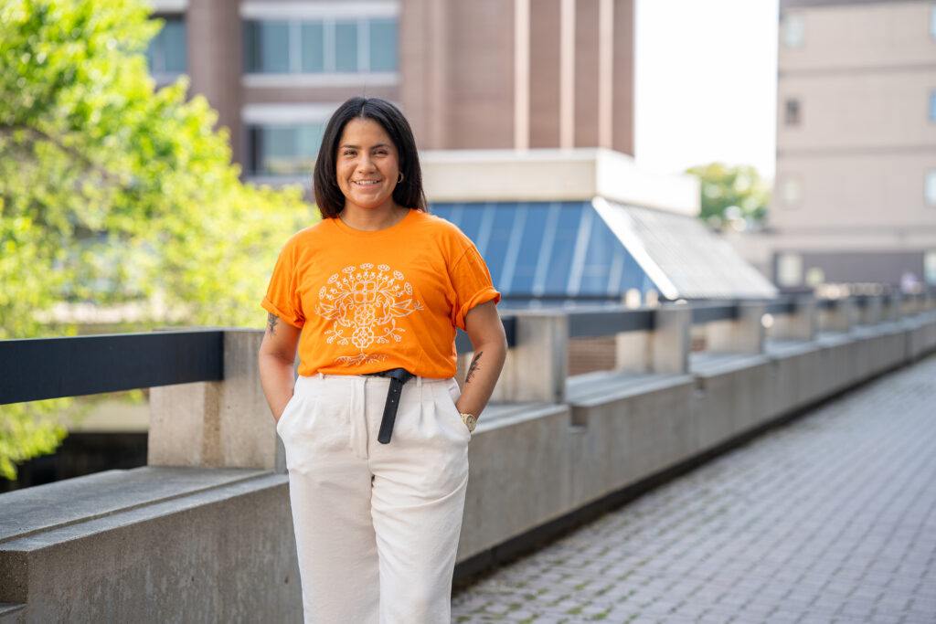 e8体育网E8体育比分 Leticia Spence 穿着她为 2023 年橙色衬衫日设计的衬衫，站在圣母院校园外。