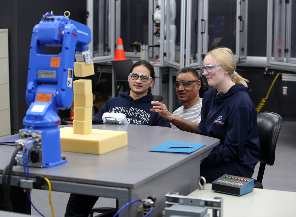 男女学生与 e8体育 讲师一起操作机械臂。