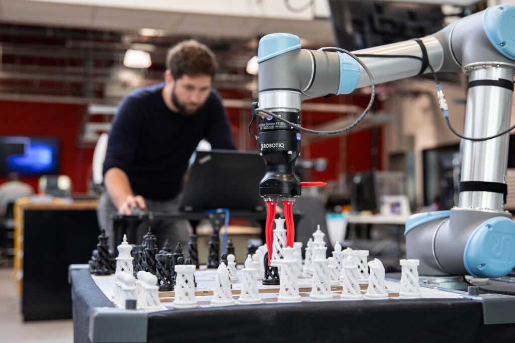 男性 e8体育 研究员通过控制来移动抓住棋子的机械臂。