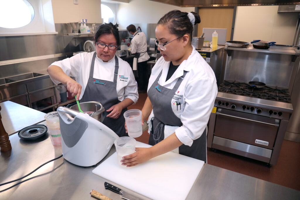 身穿厨师服和围裙的土著妇女在 e8体育 的草原研究厨房内搅拌食材