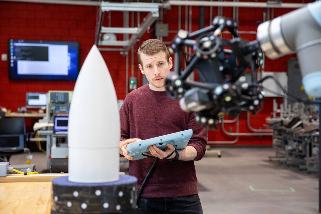 穿栗色毛衣的男人使用电脑面板控制机械臂。