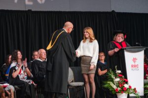RRC Polytech graduate Kate Rudnyk shakes hands with RRC Polytech president Fred Meier, onstage at convocation ceremony.