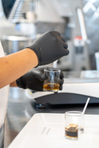 Close-up of gloved hands stirring small jar of honey, with second jar on a counter.