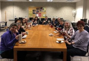 图书馆工作人员围坐在会议室桌子旁，举着可重复使用的咖啡杯。