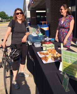 两个人，其中一个骑着自行车，在外面的桌子旁笑着，桌上摆着糕点、果汁和水。