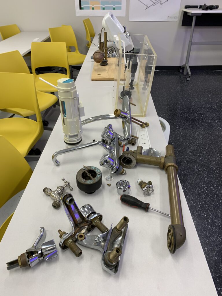 桌子上铺着各种水龙头、盥洗用品和其他管道用品。