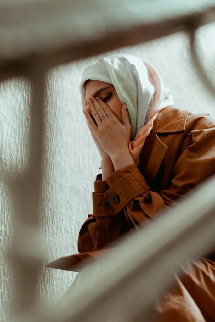 一个戴着头巾、穿着外套、双手捂脸哭泣的女人。