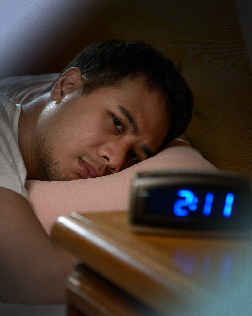 一个男人把脸放在枕头上，失望地看着时钟。时钟上的时间是凌晨 2:11。