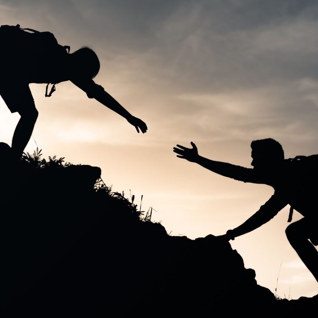 一名徒步旅行者向另一名徒步旅行者伸出手来帮助他们上坡。